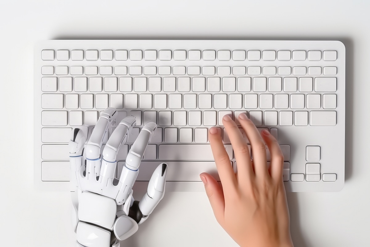 Human and robot hand typing side by side on keyboard